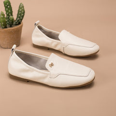 Mocasines retro con detalle de lazo metálico, estilo relajado, en negro, blanco y gris.